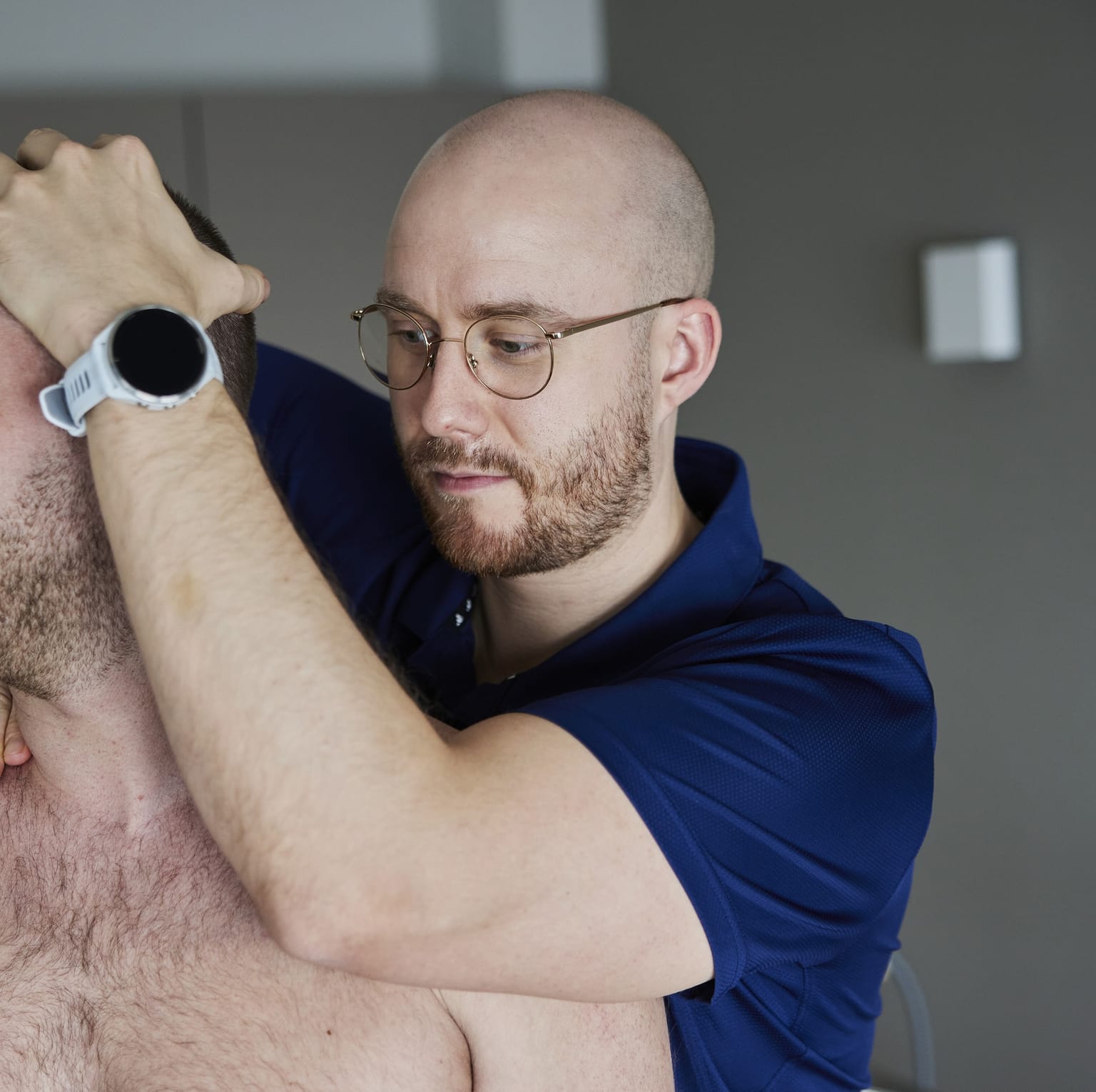 Osteopath mobilisiert mit beiden Händen die obere Halswirbelsäule eines sitzenden Patienten