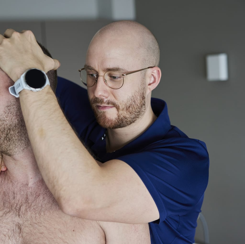 Osteopath mobilisiert mit beiden Händen die obere Halswirbelsäule eines sitzenden Patienten