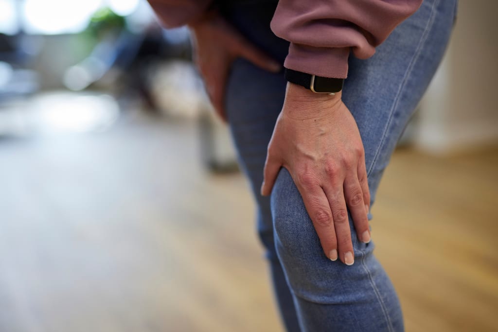 Eine Frau fasst sich im Stehen mit der Hand an das schmerzende Knie