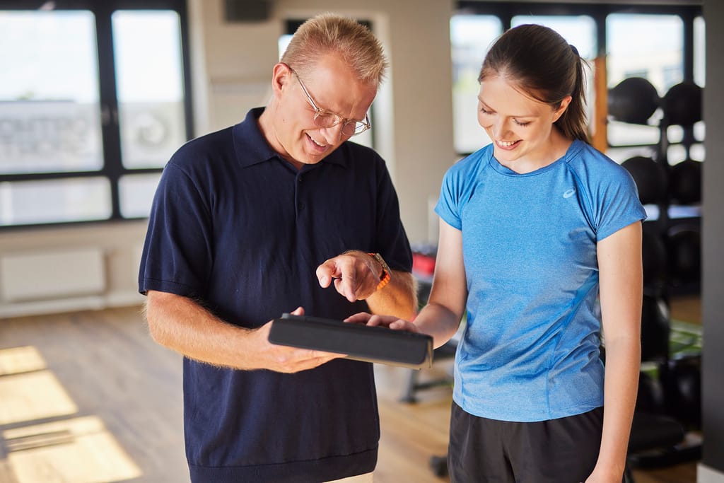 Arzt und Patientin besprechen auf einem Tablet den Trainingsfortschritt im Trainingsraum der Praxis