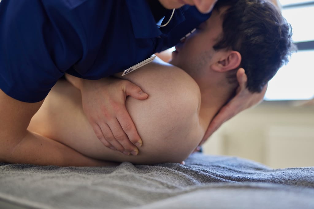 Ein Osteopath behandelt mit der Hand den oberen Rücken und das Schulterblatt eines seitlich liegenden Patienten